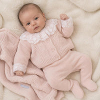 Bebê usando body branco com gola de renda por baizo de casaco de tricot rosa
